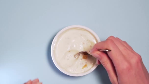 A person eats a spoonful of gluten-free vegetarian yogurt with fresh fruits. Female hands scooped a spoon of yogurt on a white background isolated - Filmati, video