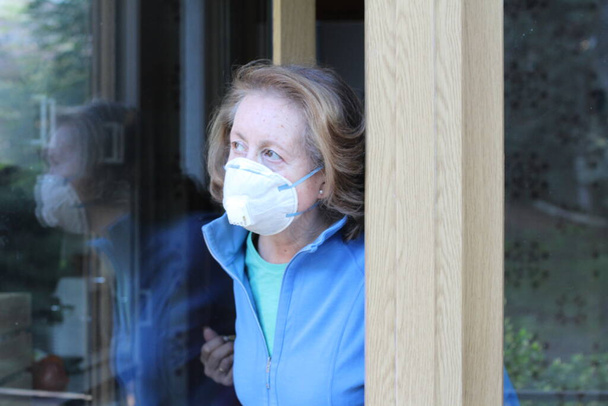 close-up portrait of beautiful mature woman in medical protective mask looking out of window - Photo, Image