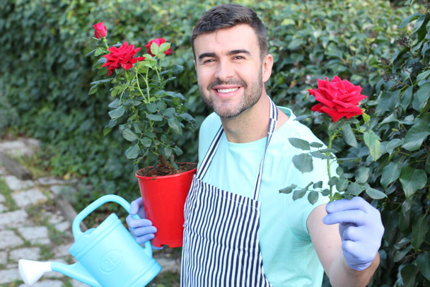 赤いバラと庭のポットを持つハンサムな若い男のクローズアップ肖像画 - 写真・画像