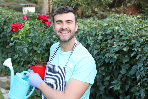 portrait en gros plan de beau jeune homme avec des roses rouges et un pot d'arrosage dans le jardin
 - Photo, image