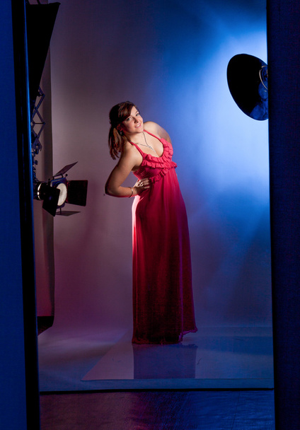 Young girl in long red dress posing in studio against flashes - Foto, imagen