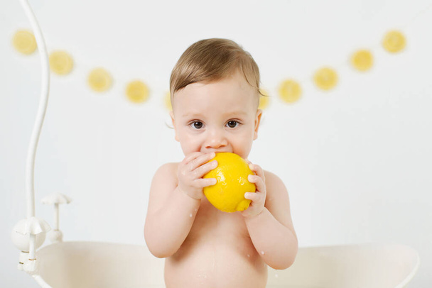  Милый милый малыш, принимающий молочную ванну с лимонами и лаймами. Мальчик ест лимоны на белом фоне
. - Фото, изображение