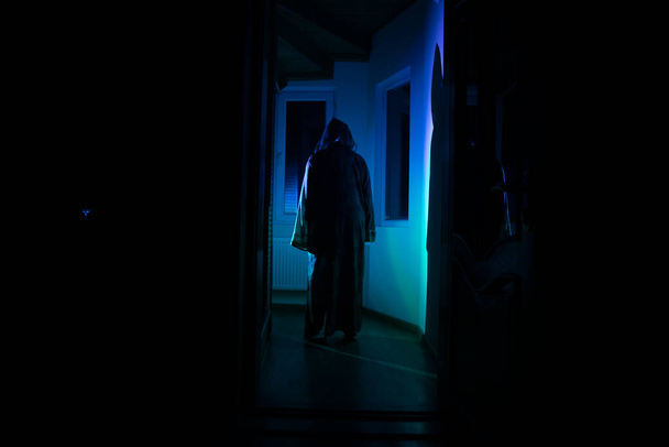Silueta de una figura de sombra desconocida en una puerta a través de una puerta de cristal cerrada. Chica silueta espeluznante en la noche con humo en el fondo - Foto, imagen