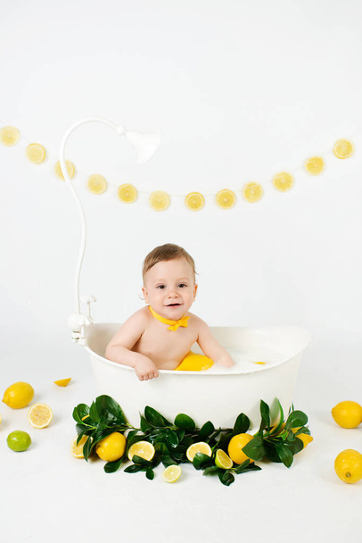  Netter entzückender kleiner Junge mit Milchbad mit Zitronen und Limetten. Junge, der Zitronen auf weißem Hintergrund isst. - Foto, Bild