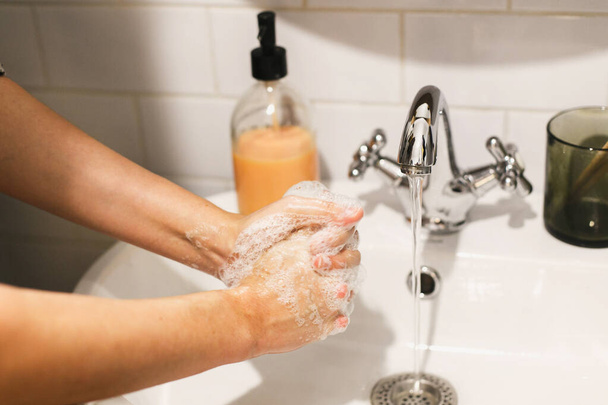 Washing hands. Hands washing with soap foam on background of flowing water in bathroom. Rubbing palms. Prevention of flu disease. Personal hygiene. Cleaning hands to prevent coronavirus epidemic - Photo, Image