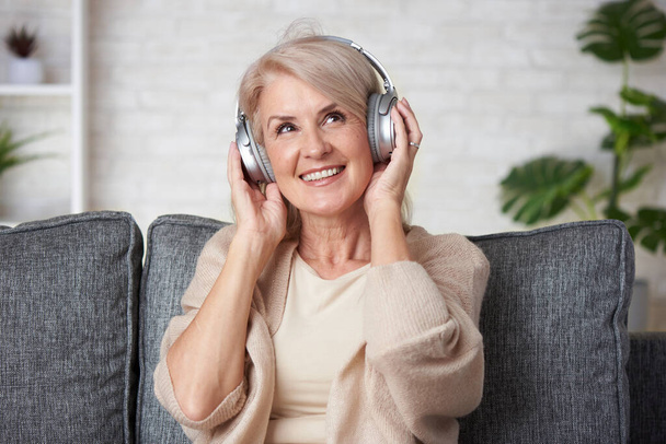 Senior old woman listening to her favourite music through big headphones - Foto, Imagem