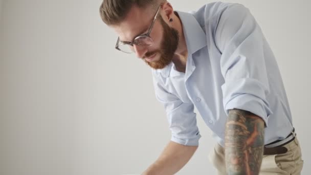 A focused young bearded man wearing a shirt is working with documents in the white office - Video