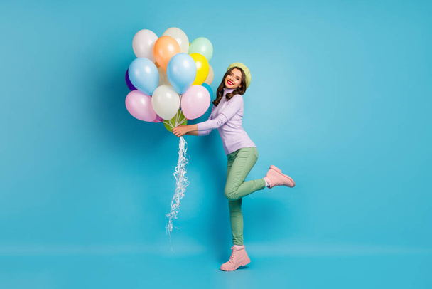 Full body photo of pretty funny lady bring many colorful air balloons friends event party wear purple sweater beret cap green pants shoes isolated blue color background - Foto, Imagem