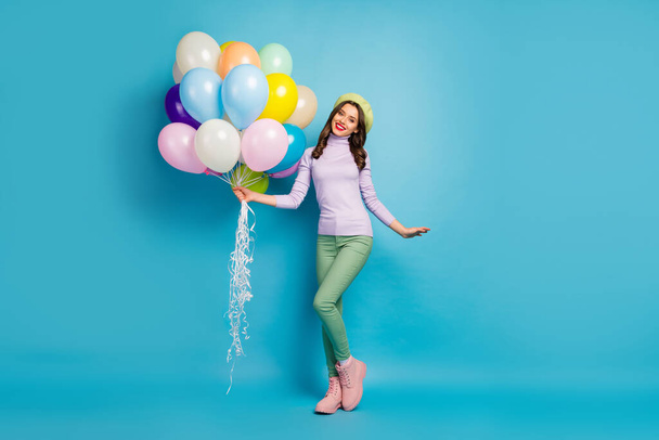Full length photo of pretty funny lady bring many colorful air balloons friends event party wear purple sweater beret cap green pants footwear isolated blue color background - Foto, Bild