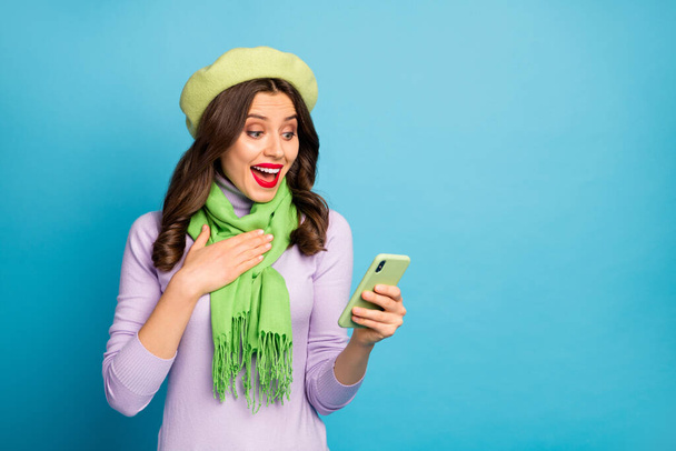 Photo of amazed crazy lady hold telephone read post comments new followers subscribers wear green beret purple turtleneck scarf pants isolated blue color background - Foto, imagen