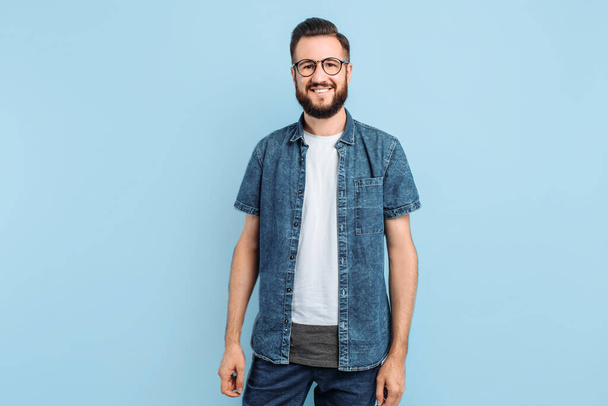 Homme intelligent attrayant dans des lunettes, dans des vêtements décontractés posant debout sur un fond bleu isolé
 - Photo, image