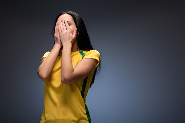 frightened female football fan covering face on grey  - 写真・画像
