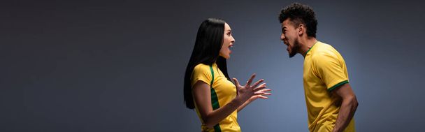 tiro panorâmico de casal multicultural de fãs de futebol animado em camisetas amarelas gritando em cinza
 - Foto, Imagem