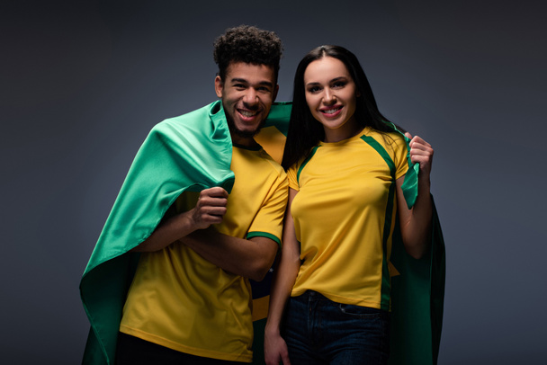 monietninen pari onnellisia jalkapallofaneja, joilla on brasilialainen lippu harmaalla
 - Valokuva, kuva