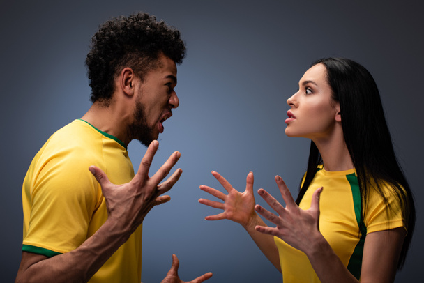 agressivo casal multicultural de fãs de futebol em camisetas amarelas gesticulando e gritando em cinza
 - Foto, Imagem