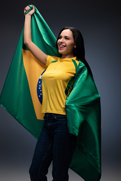emotional female football fan wrapped in brazilian flag on grey - Fotografie, Obrázek