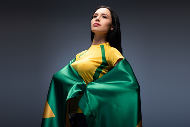 attractive proud female football fan wrapped in brazilian flag on grey - Foto, afbeelding