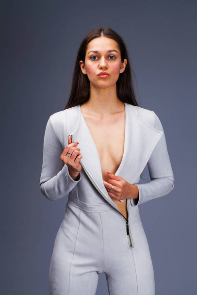 Sexy fashion brunette woman in gray leather suit posing in the studio on a gray background - 写真・画像