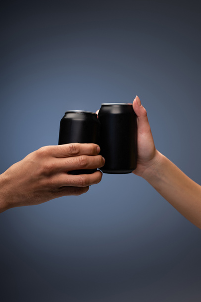 cropped view of man and woman clinking with black cans on gray - Photo, image