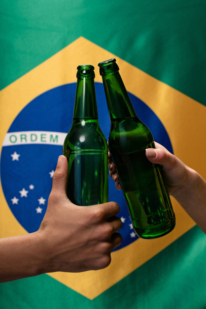 vue recadrée du couple de fans de football cliquetis avec des bouteilles de bière avec drapeau brésilien derrière
 - Photo, image
