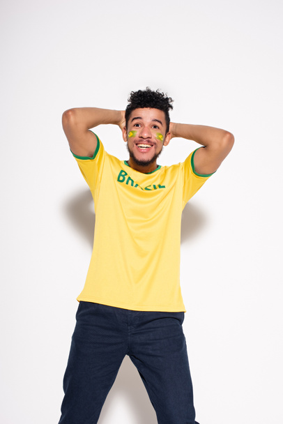 fröhlicher afrikanisch-amerikanischer Fußballfan in gelbem T-Shirt mit brasilianischem Schriftzug auf grau - Foto, Bild