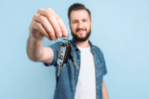 Surprised excited happy man with a beard holding car keys in his hands, standing on an isolated blue background - Foto, Imagem