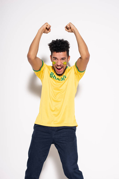 Афріканський футбольний фанат у жовтій футболці з бразільським знаком, який кричить і жестикує на сірому - Фото, зображення