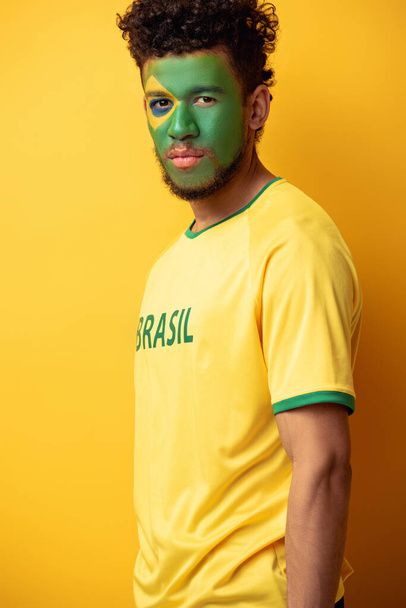ハンサムなアフリカ系アメリカ人のサッカーファン顔は黄色にブラジルの旗として描かれている - 写真・画像