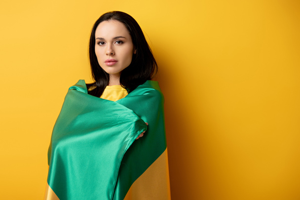 beautiful female football fan wrapped in brazilian flag on yellow - Photo, Image