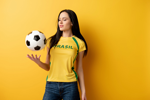 attractive female football fan throwing up ball on yellow - Valokuva, kuva