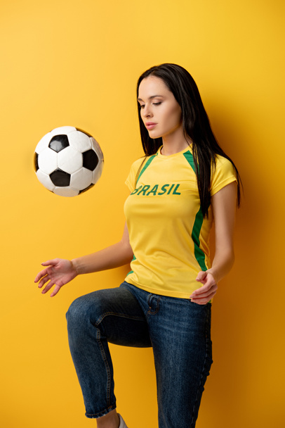 concentrated female football fan kicking ball on yellow - Фото, зображення