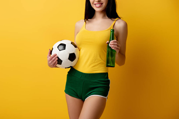 黄色のボールとビールを持っている女性サッカーファンのクロップドビュー - 写真・画像