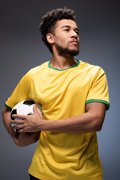 fier fan de football afro-américain en t-shirt jaune tenant le ballon sur gris
 - Photo, image