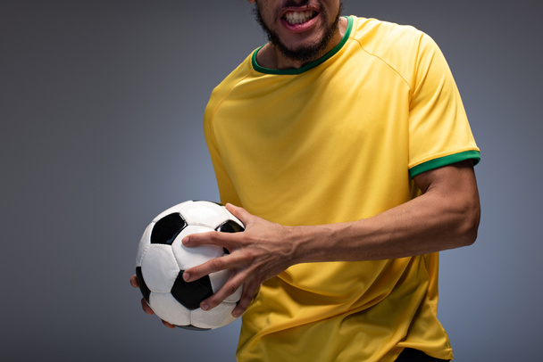 cropped view of emotional football fan in yellow t-shirt holding ball on grey - Foto, afbeelding