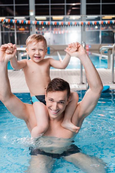 szczęśliwy trener pływania gospodarstwa słodkie dziecko maluch na ramionach w basenie  - Zdjęcie, obraz
