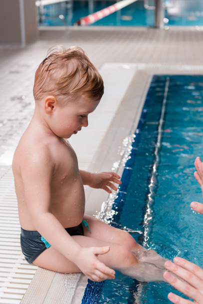 スイミングプールのかわいい幼児の男の子の近くで泳ぐコーチのクロップドビュー  - 写真・画像