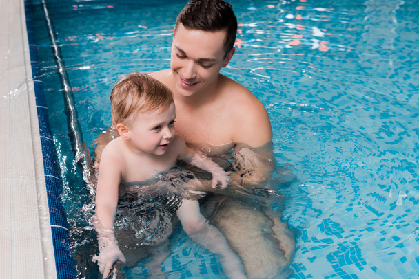 Χαρούμενος εκπαιδευτής κολύμβησης που διδάσκει μικρό παιδί στην πισίνα  - Φωτογραφία, εικόνα