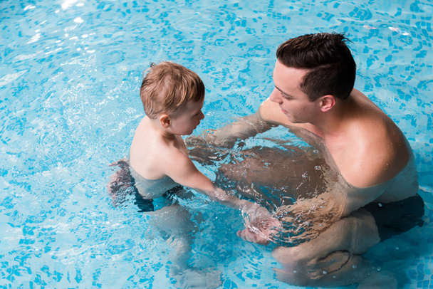 overhead view of happy swim trainer teaching toddler kid in swimming pool  - Foto, afbeelding