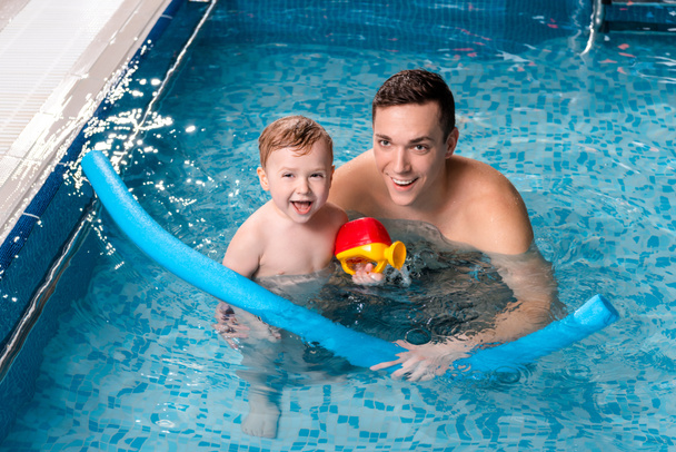jóképű úszó edző mosolyog kisfiúval a medencében  - Fotó, kép