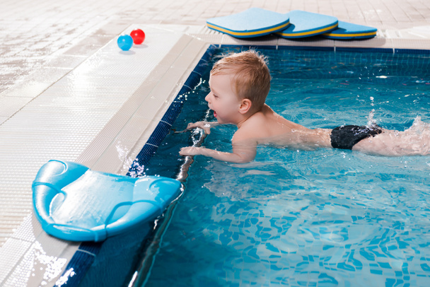 幸せな幼児の男の子水泳プールのフラッターボードの近くで泳ぐ  - 写真・画像