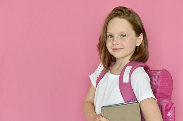 little cute school girl with backpack holding books isolated on pink background  - Fotografie, Obrázek