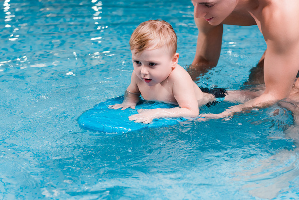 toddler boy swimming with flutter board near swim coach  - Fotó, kép