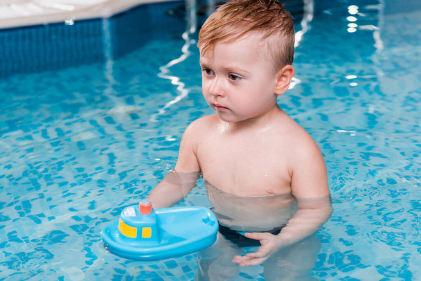 Niedlicher Kleinkind Junge spielt mit Spielzeugschiff im Schwimmbad  - Foto, Bild