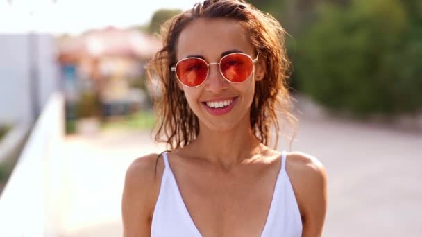 radośnie uśmiechnięta Piękna młoda opalona multyetniczka w białym bikini i różowych okularach przeciwsłonecznych - Materiał filmowy, wideo