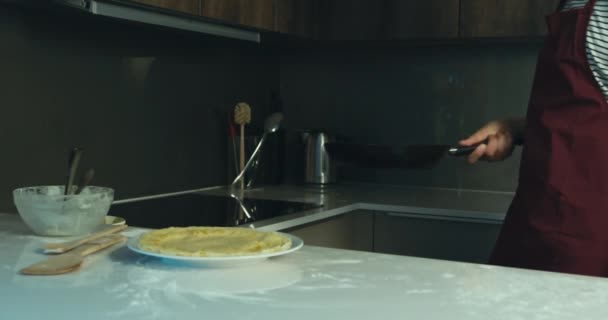 A young man is flipping a pancake in his kitchen, then decides to flip it again - Materiał filmowy, wideo