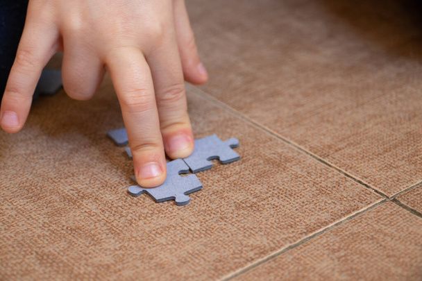 Kinderhand sammelt Rätsel auf dem Fußboden auf brauner Fliese - Foto, Bild