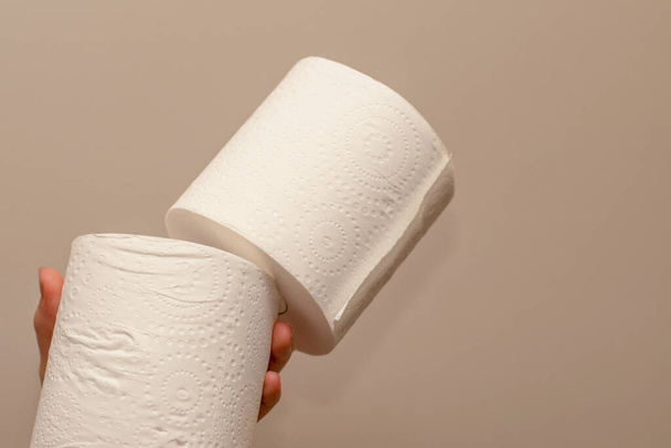 Cierre de manos con dos rollos de papel higiénico sobre fondo neutro. Concepto de escasez y acumulación
 - Foto, imagen