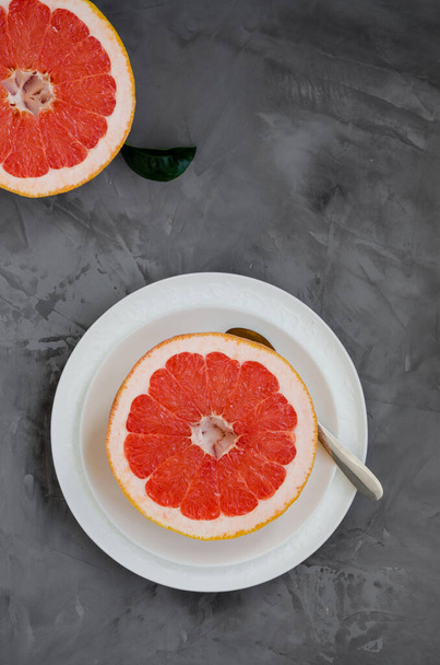Frisch reife saftige Hälfte der Grapefruit auf einem Teller mit einem Löffel auf dunklem Betongrund. Gesunde Brotzeit. Vertikale Orientierung - Foto, Bild