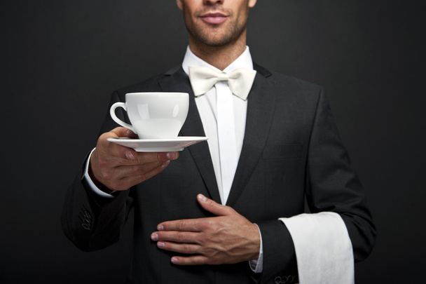 Офіціант у костюмі тримає чашку кави
 - Фото, зображення