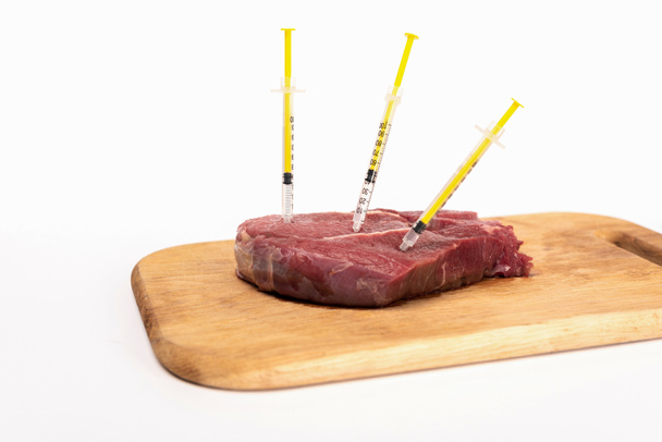 Syringes in raw meat on wooden chopping board isolated on white - Photo, Image